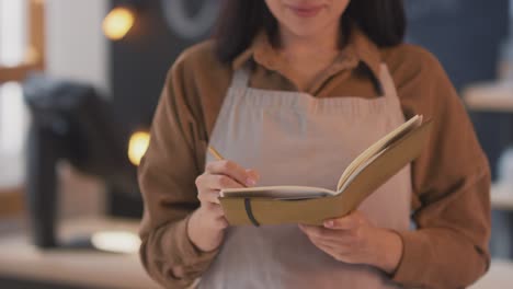 Camera-Focuses-On-The-Face-Of-An-Waitress-In-A-Coffee-Shop-Who-Takes-Notes-In-A-Notebook,-Looks-At-The-Camera-And-Smiles