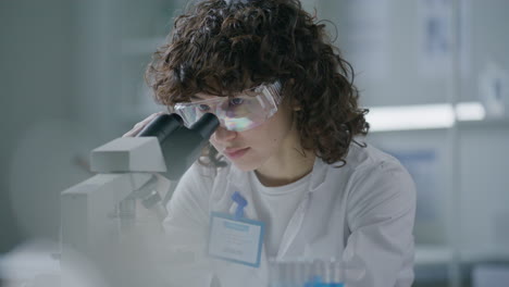 young female scientist observing specimen under microscope in laboratory