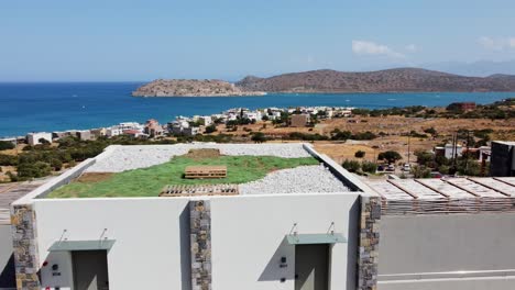 View-of-the-sea-at-CayoResort-in-Greece-Crete---Brunette-woman-in-swimming-costume-sits-at-the-pool-edge-and-drinks-cocktail---Drone-flies-forwards-towards-the-sea