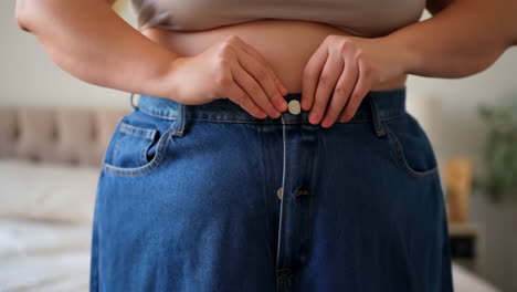 person struggling to button up tight jeans