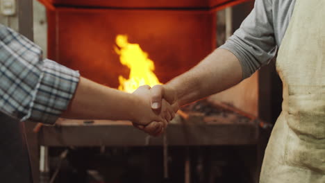 two blacksmiths shaking hands and bumping fists at work