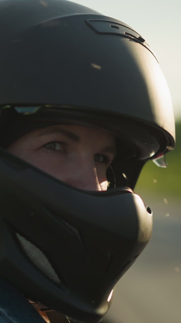 Close-up side view of a woman wearing a matte black helmet, looking contemplatively ahead, a small flying insect is visible near her face