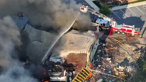 firefighter on ladder extinguish fire after gas explosion during daytime - dark dense fumes rising up