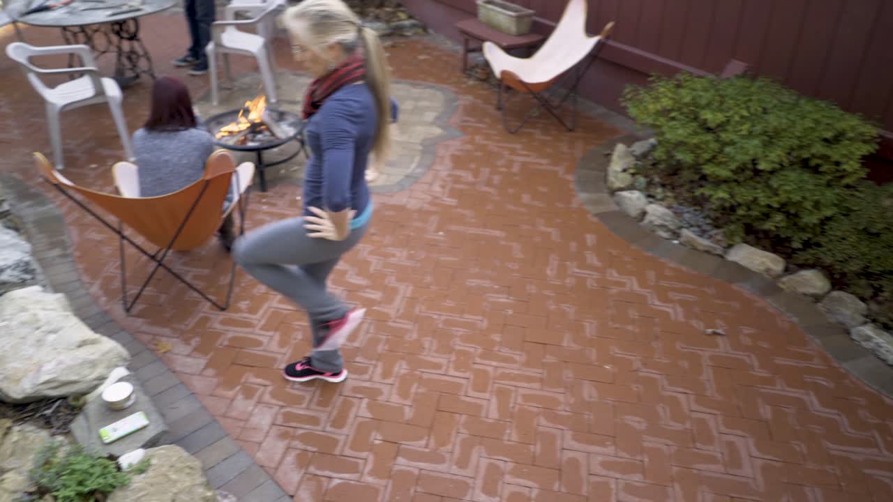 With outstretched arms a mature blonde woman practices middle eastern folk dance on her patio.