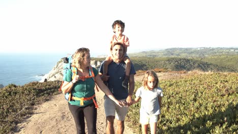 Happy-couple-of-parents-and-children-walking-on-path-at-sea