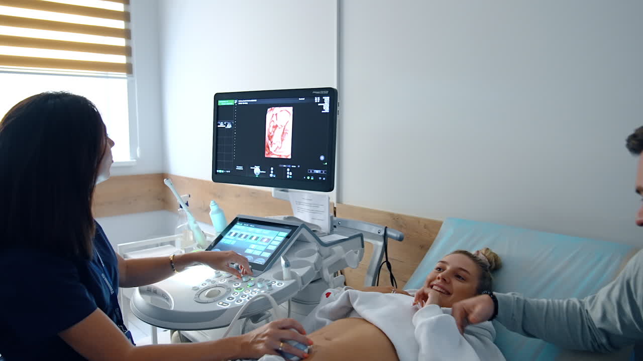 Young future parents are undergoing pregnancy examination. People are excited to see their baby image on the screen.