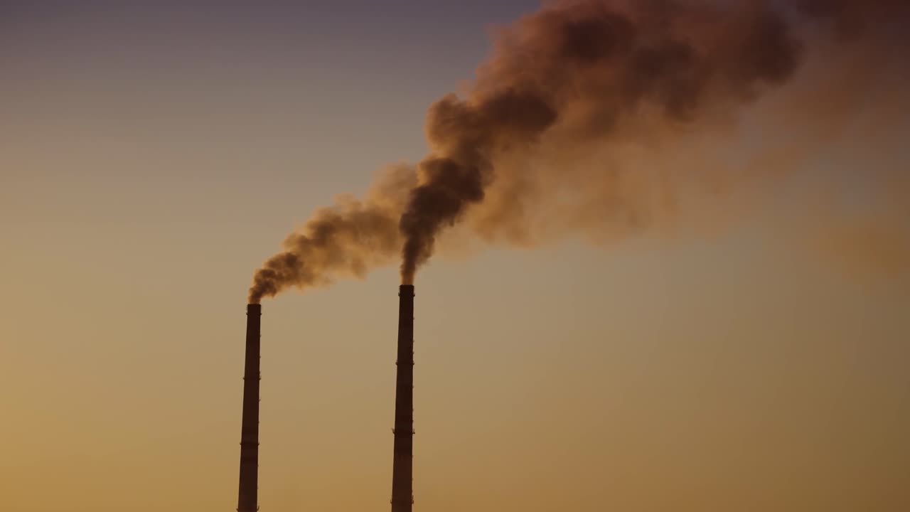 Air pollution by smoke coming out of two factory chimneys. Aerial view.