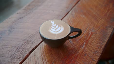 Paralaje-De-Mano-De-Arte-Latte-En-Taza-De-Té-Negra-Con-Hojas-Blancas-En-El-Café