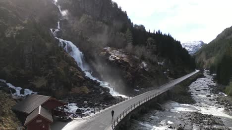 drone shot of male tourist walking on bridge under the latefoss waterfall, norway