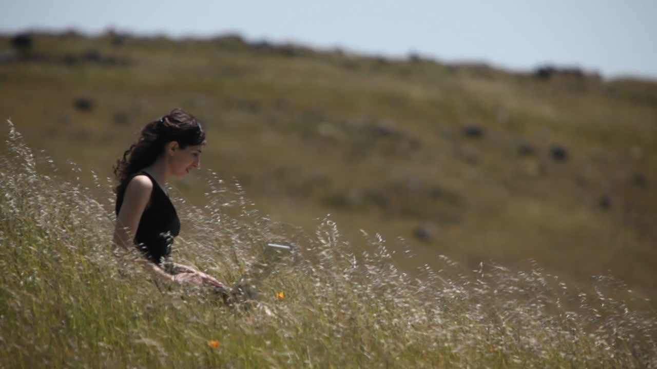 노트북을 사용하는 여성이 들판에 앉아 있다