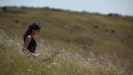 A-woman-using-a-laptop-sits-in-a-field