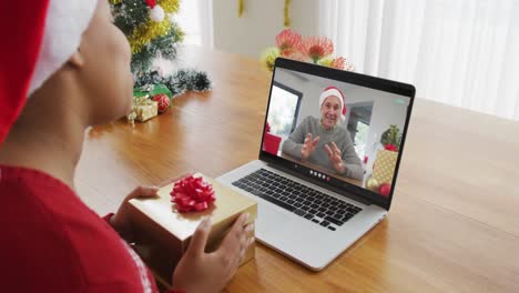 Mujer-Afroamericana-Con-Gorro-De-Papá-Noel-Usando-Una-Computadora-Portátil-Para-Una-Videollamada-Navideña,-Con-Un-Hombre-En-La-Pantalla