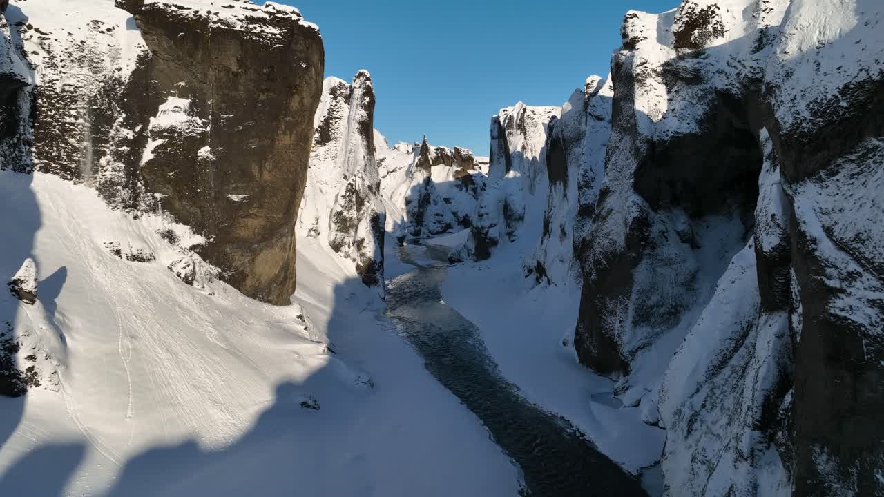 vista aérea a través de un cañón cubierto de nieve, sobre un río glaciar que fluye, en una noche soleada