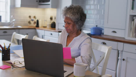 mujer afroamericana de alto nivel pegando notas en su computadora portátil en casa