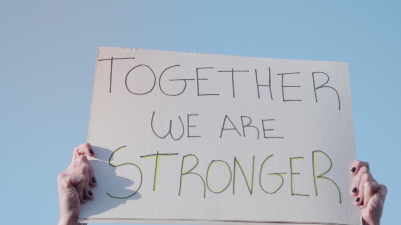 Hands Holding 'Together We Are Stronger' Protest Sign Against Blue Sky