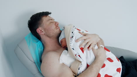 smiling happy man holding and soothing his newborn baby on the chest. skin to skin contact.