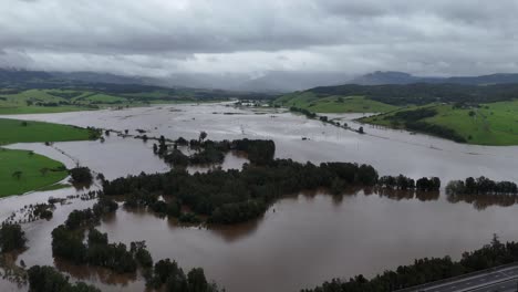gerringong under floodwaters with visible farmland, trees, and infrastructure affected by storm, panoramic establishing aerial drone