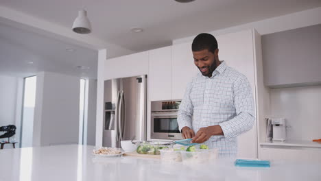 Hombre-En-La-Cocina-Preparando-Comida-Rica-En-Proteínas-Y-Poniendo-Porciones-En-Recipientes-De-Plástico