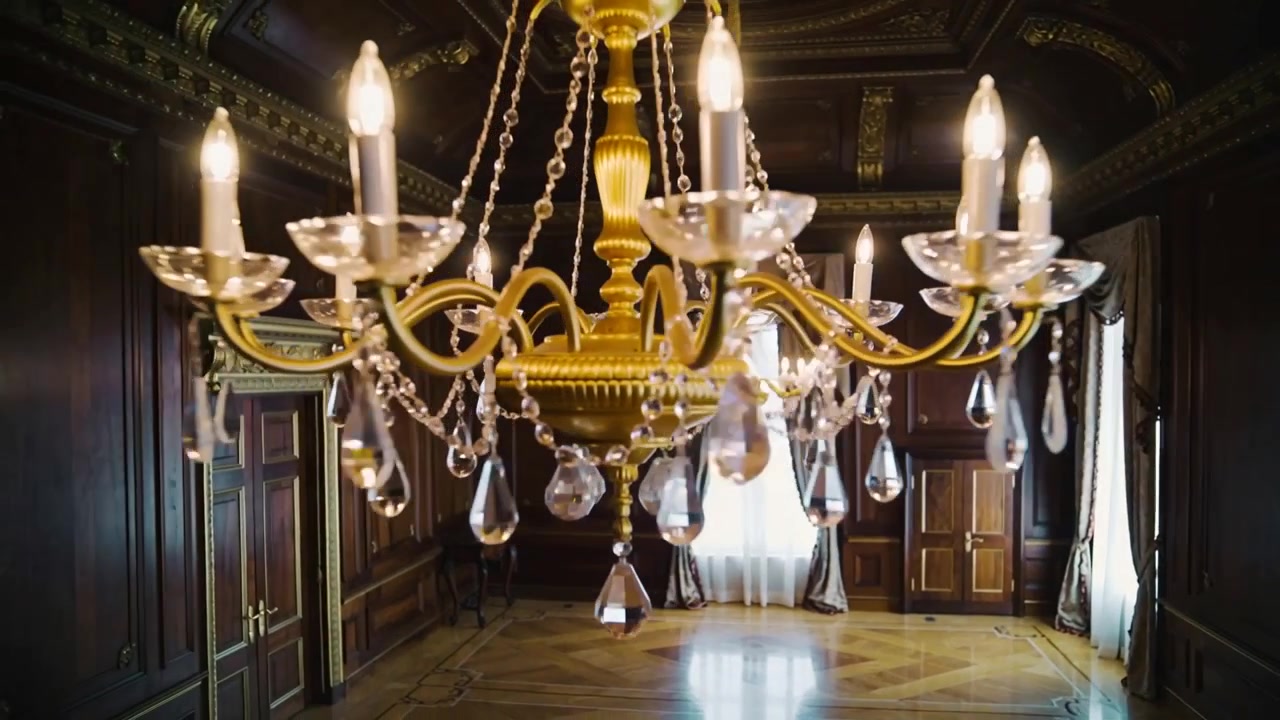 Zooming camera pushing closer to large gold crystal chandelier in ornate parlor, revealing details