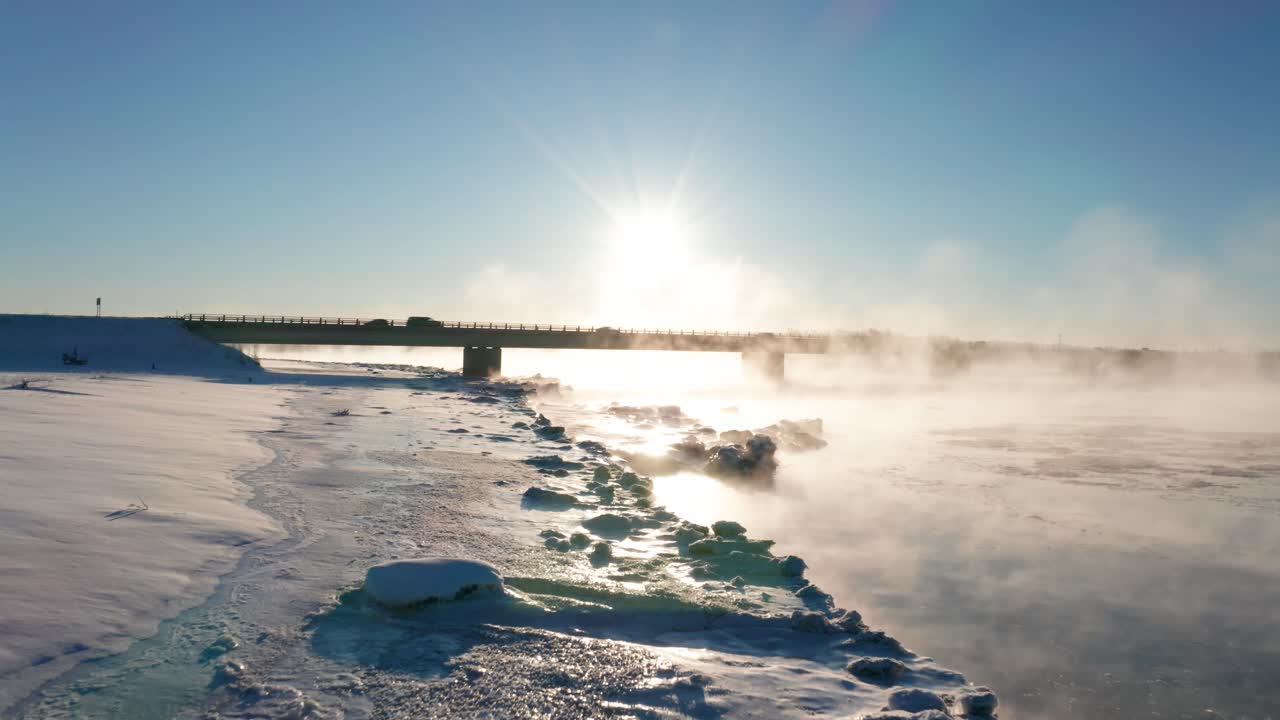 Winter wonderland with a snowing cold river, clear skies, and misty fog rolling over the Kenai River in Alaska with Mountains in the background