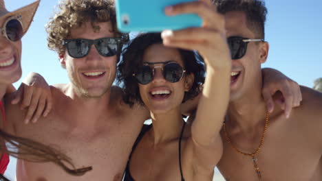 mixed race group of friends taking selfies on the beach using phone camera