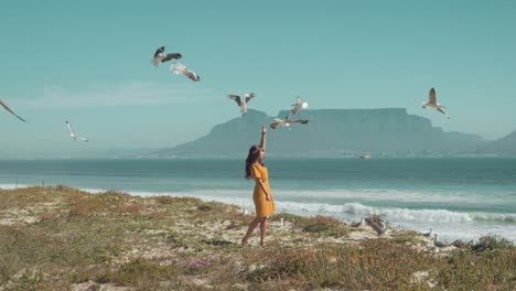 playful woman feeding seagulls on beach in iceland, as they swoop down against clear blue sky, creating peaceful and lively scene