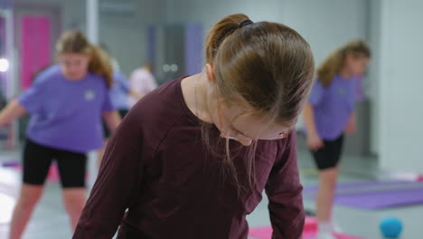 young kids actively engaged in a fitness workout session, focusing on exercises one glasses concentrating on her movement while others in the background participate in gym activities