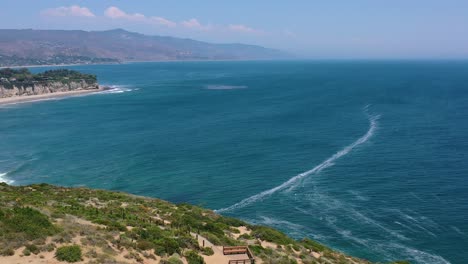 low-altitude-aerial-drone-flying-past-a-large-peninsula-hill-panning-towards-the-empty-Malibu-Hills-coastline-of-California-USA-and-empty-beach-below-as-the-Pacific-Ocean-waves-crash-below