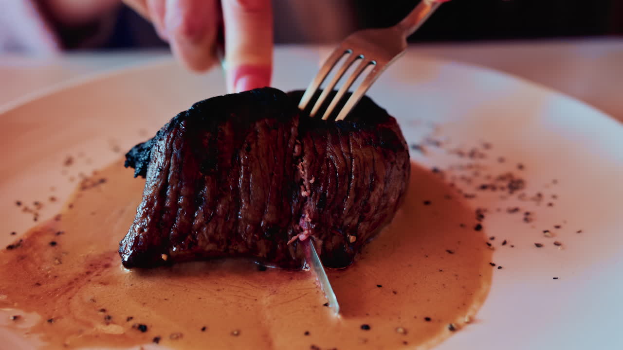 Primo piano di mani che tagliano una succosa bistecca alla griglia servita con salsa cremosa