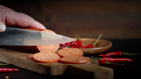 male hands slicing a stick of salami into pieces.