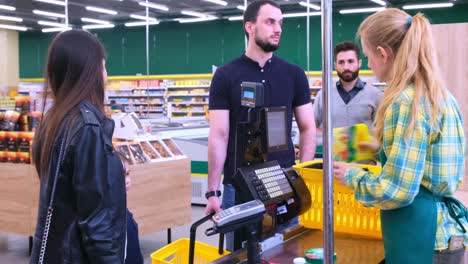a young cashier assists customers at a busy checkout, showcasing the vibrancy and interaction of retail shopping experience in a modern grocery store environment