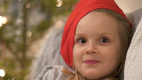 portrait of cute and happy four year old girl in santa claus hat smiling mischievously, christmas elf concept