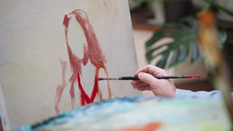 artist draws woman in red dress in studio closeup. man makes acrylic paint strokes on canvas creating art workshop. master at painting in shop