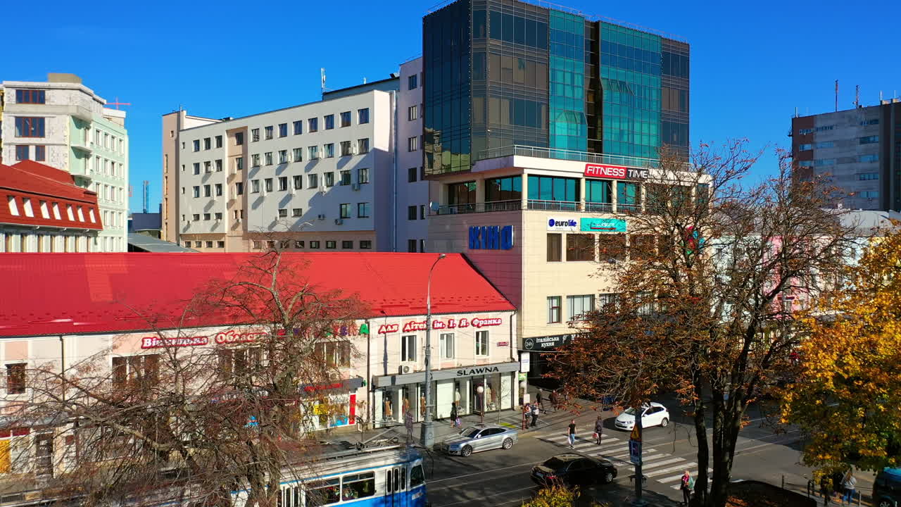 Trams go by the busy road downtown. People walking and resting in the city centre. Drone rising over the urban panorama.