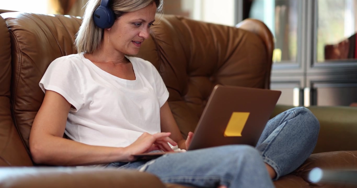 Donna con le cuffie su un divano con un laptop, primo piano