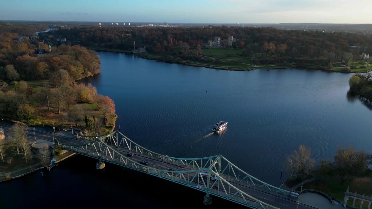 Ponte di Glienicke con auto e una casa galleggiante che attraversano il fiume Havel a Berlino, Germania, durante una soleggiata giornata autunnale. Spettacolare vista aerea con drone.