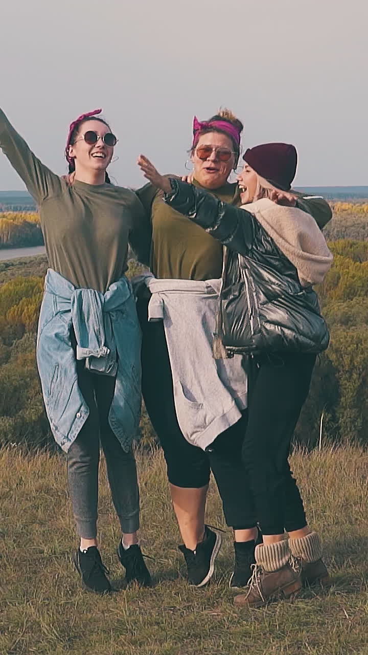 tipsy ladies jump and raise hands with happiness at blue camp tent on green river bank in autumn slow motion