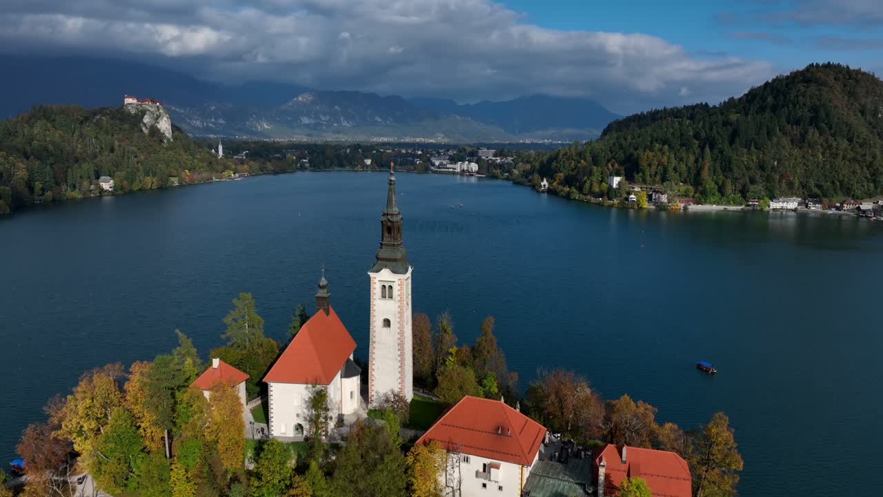 Veduta aerea centrata dell'Isola di Bled e della chiesa con montagne sullo sfondo, inquadratura media.