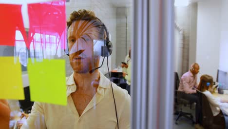 ejecutivo masculino hablando en auriculares mientras busca nota adhesiva 4k