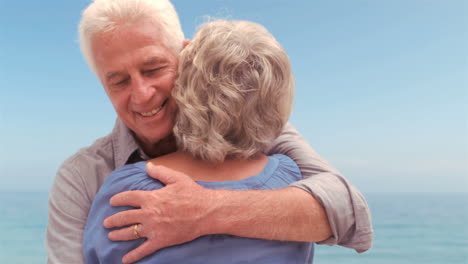 una pareja de mayores sonrientes abrazándose.