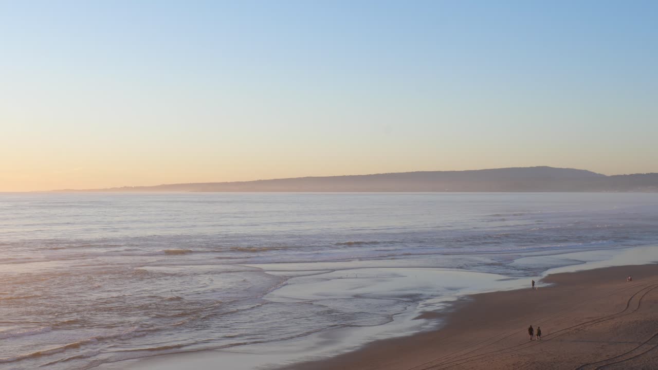 Beautiful sunset looking over Santa Cruz beach with mountains in the background. People walking on beach during sunset