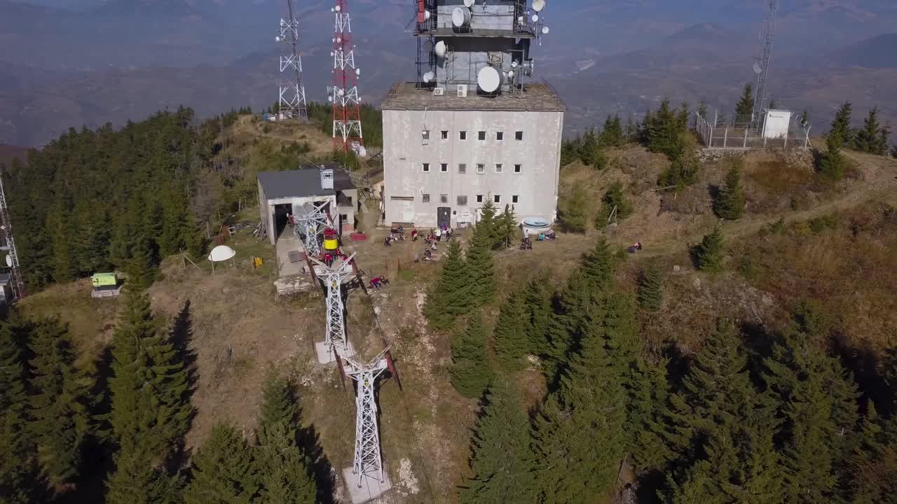 cumbre heniu, rumania - un edificio en la cima de la montaña con una torre de telecomunicaciones en la parte superior, torres eléctricas cercanas rodeadas de pinos verdes - toma aérea de drones
