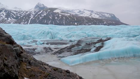 static, shot of the coast of the turquoise, skaftafellsjokull glacier, snowy mountains in the background, on a cloudy day, in south coast of iceland