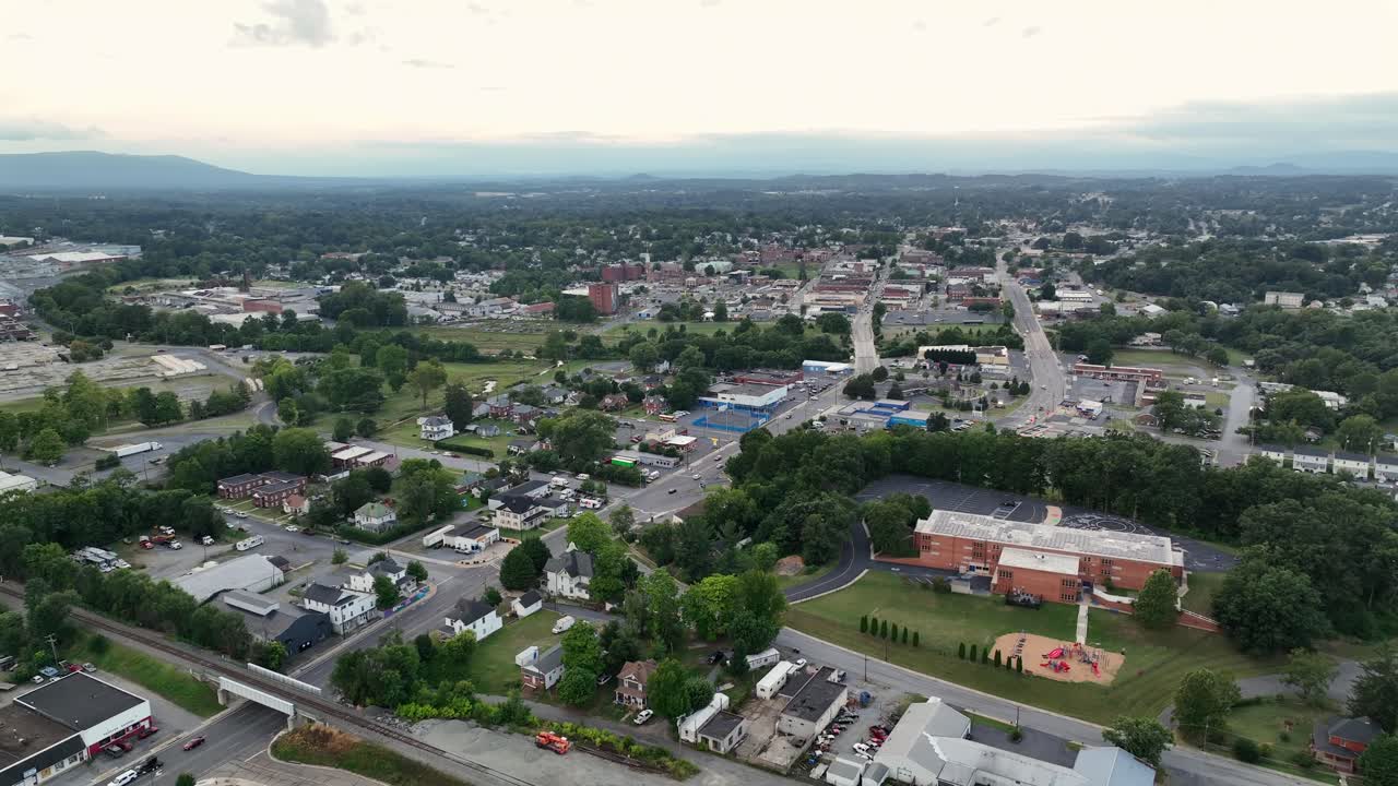 Aerial rising shot of red brick Wenonah Elementary Schoolin suburb of waynesboro, Virginia. Traffic on road, along gas station and railway tracks with parking wagons. Sunny summer day