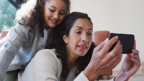 Happy-mixed-race-mother-and-daughter-laying-on-the-floor,having-fun-and-taking-selfie