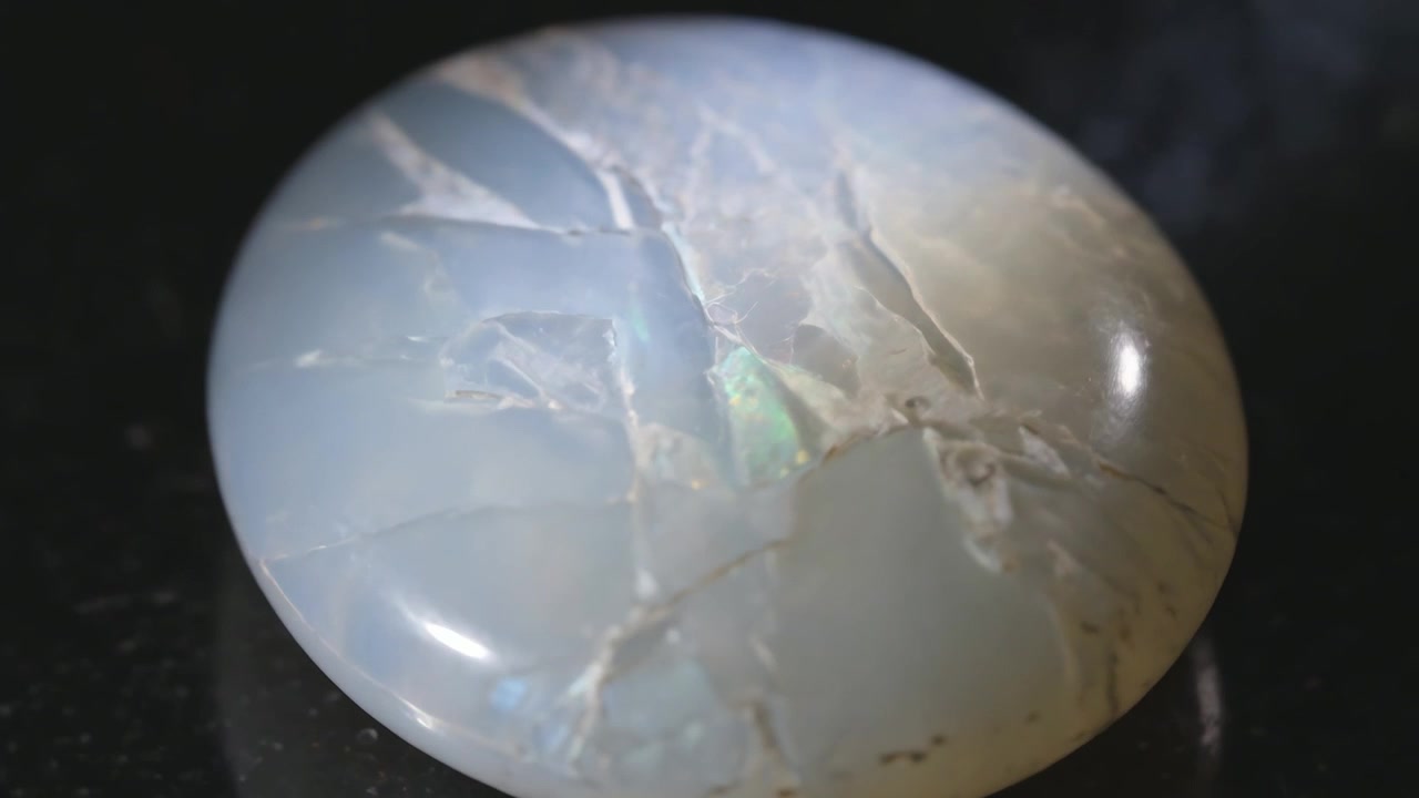 Luce mutevole che rivela una gemma di opale lattiginoso che lampeggia verde e poi blu su base nera, mostrando iridescenza