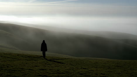person walking on a grassy hill in foggy weather