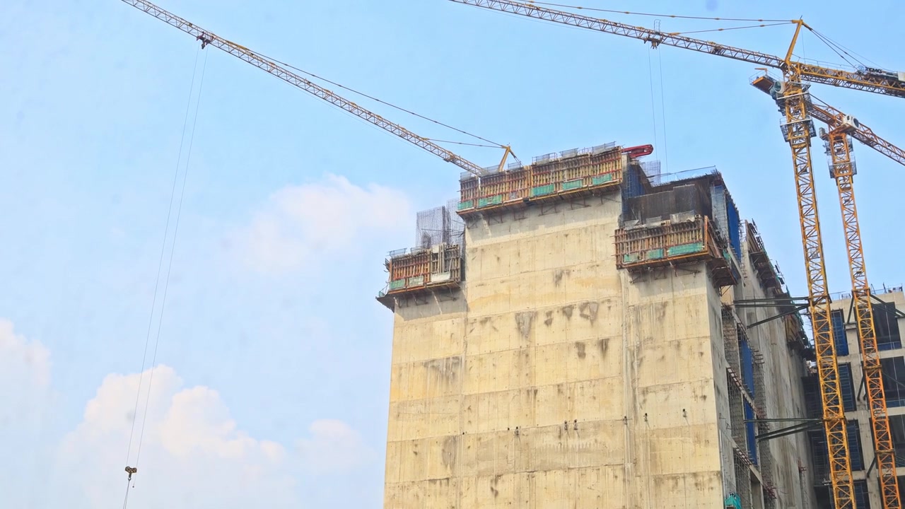 Toma panorámica de grúa torre elevando materiales junto a una estructura de hormigón de gran altura.