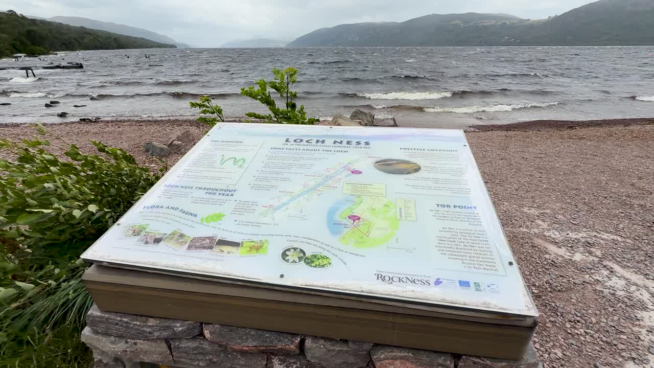 Tourist information sign by Loch Ness beach, camera slowly panning, overcast natural daylight, scenic view