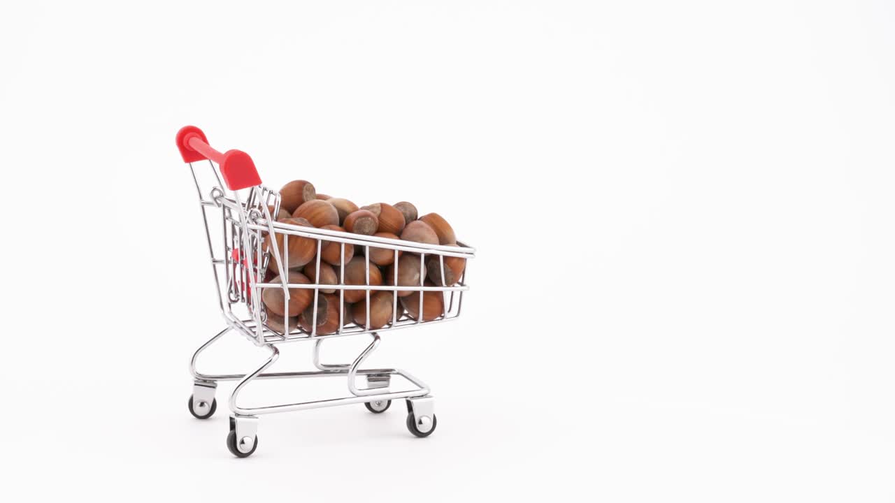 Wózek sklepowy wypełniony orzechami laskowymi poruszający się do przodu. Izolowany na białym tle. Zbliżenie. Makro.